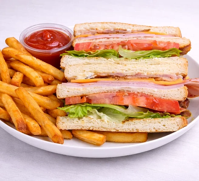 Clubhouse sandwich with fries and a cup of ketchup on a white plate