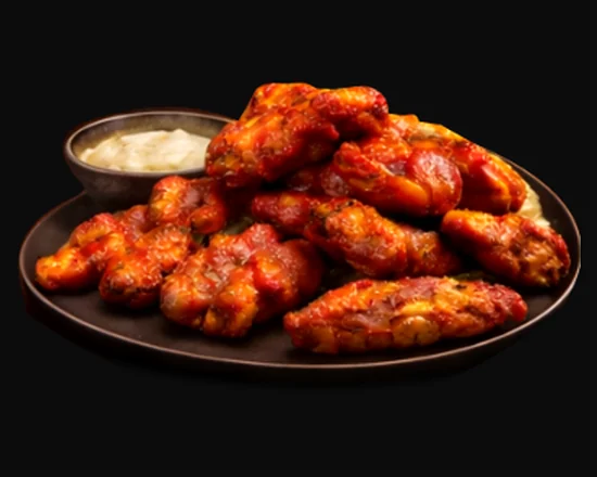 Saucy chicken wings on a plate with a cup of dip
